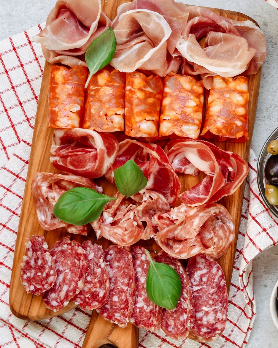 food antipasto prosciutto ham, salami, olives and bread and tomato and basil bruschetta charcuterie board two glasses of white wine or prosecco